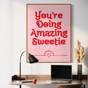 Puede incluir: P&oacute;ster motivacional rosa con el texto "You're Doing Amazing Sweetie" en letras rojas. Un peque&ntilde;o coraz&oacute;n rojo est&aacute; dentro de un gr&aacute;fico de sol rojo en la parte inferior del p&oacute;ster.