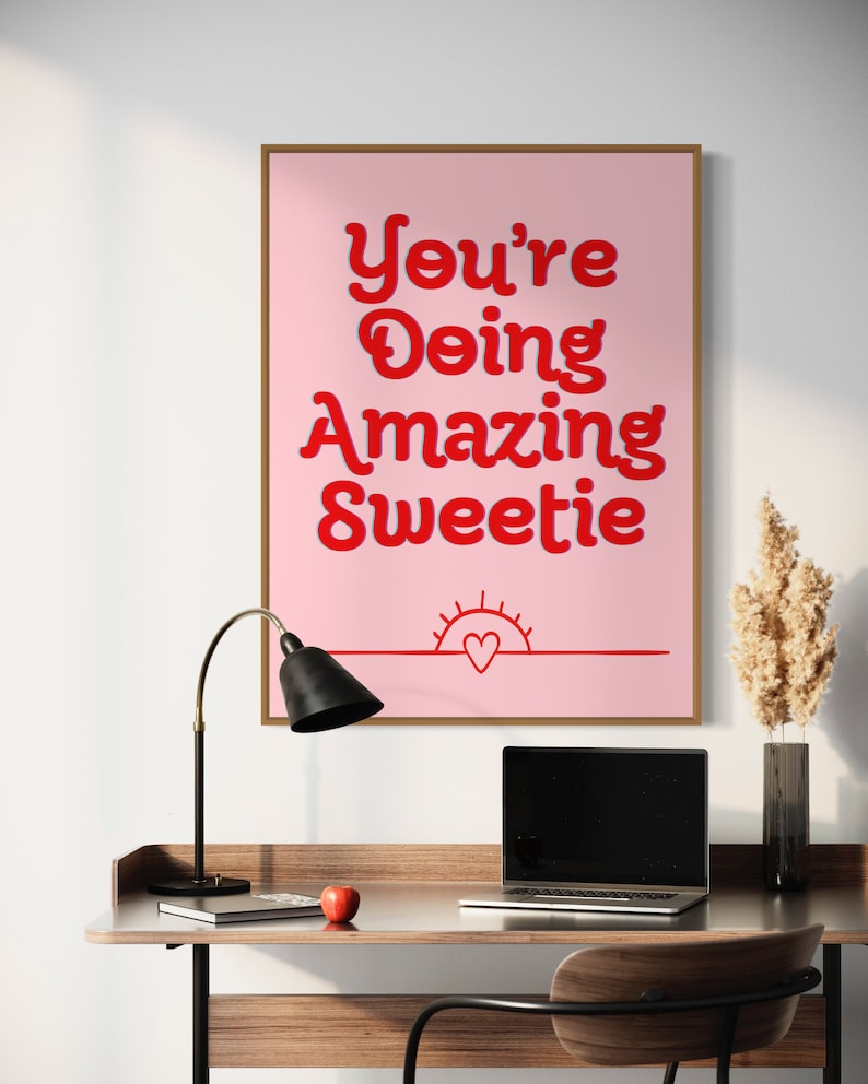 Puede incluir: P&oacute;ster motivacional rosa con el texto "You're Doing Amazing Sweetie" en letras rojas. Un peque&ntilde;o coraz&oacute;n rojo est&aacute; dentro de un gr&aacute;fico de sol rojo en la parte inferior del p&oacute;ster.