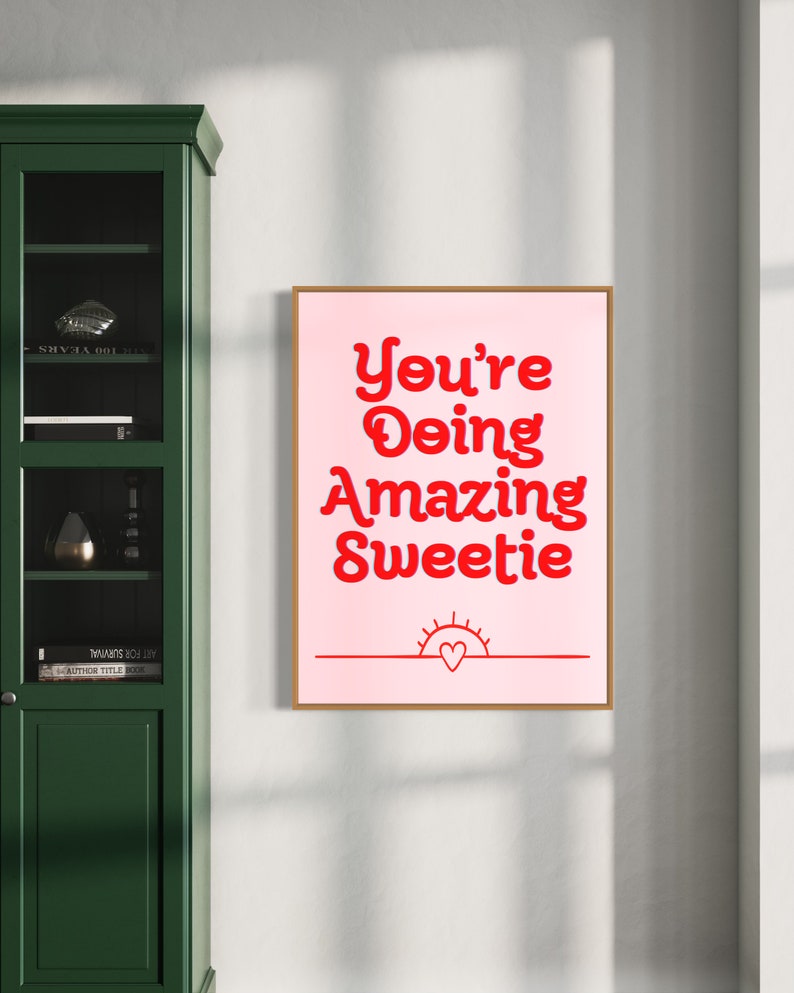 Puede incluir: Un p&oacute;ster motivacional rosa y rojo con el texto "You're Doing Amazing Sweetie" y un peque&ntilde;o sol con un coraz&oacute;n en el centro.