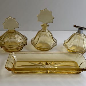 May include: A set of four amber glass vanity items, including a tray, two bottles with star-shaped stoppers, and a small jar with a star-shaped lid.