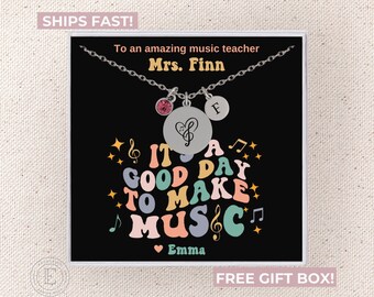 May include: A silver necklace with a music note charm and a letter F charm. The necklace comes in a gift box with a black background and the text "It's a good day to make music" in colorful retro font. The text "Emma" is also included in the design.