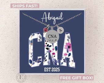 May include: A silver necklace with a floral patterned charm that says "CNA" and a small initial charm. The necklace is in a blue box with the name "Abigail" and the text "EST 2025".