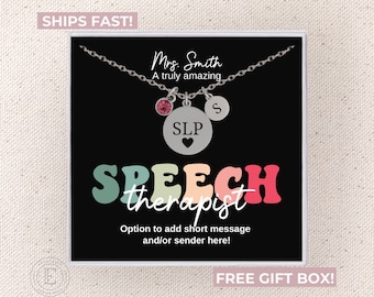 May include: A silver necklace with a pendant that says "SLP" with a heart, a pink gem, and a letter "S" charm. The necklace is on a black card with the words "Speech Therapist". The card also says "Mrs. Smith".