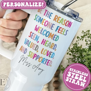 May include: White insulated tumbler with a handle and a stainless steel straw. The tumbler has a colorful text design that reads "Be the reason someone feels welcomed, seen, heard, valued, loved, and supported." The name "Miss Amy" is written below the text.