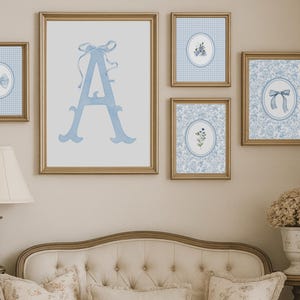 May include: A collection of framed wall art featuring a soft blue color palette. The artwork includes a large letter "A" with a bow, bow illustrations, and floral designs. The frames are gold, and the overall aesthetic is classic and elegant.