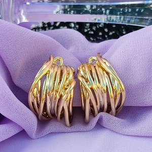 May include: A pair of gold-toned hoop earrings with a woven design. The earrings are on a purple fabric background.
