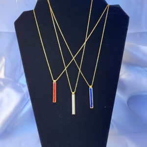 May include: Three gold necklaces with different colored bar pendants. The pendants are red, white, and blue.