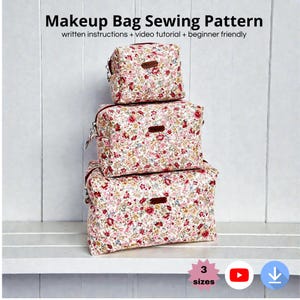 May include: Three floral print makeup bags of varying sizes are stacked on a white shelf. The bags have a white background with red and pink flowers. The text "Makeup Bag Sewing Pattern" is at the top of the image.