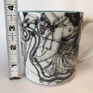 Puede incluir: Taza de cer&aacute;mica blanca con asa, con una ilustraci&oacute;n en blanco y negro de una figura mitol&oacute;gica con arco y flecha y constelaciones. La taza mide aproximadamente 7.6 cm de alto, con un borde turquesa.