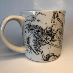 Puede incluir: Taza de cer&aacute;mica blanca con un dise&ntilde;o de constelaci&oacute;n del zodiaco en negro y dorado. La taza tiene un asa curva y un interior verde. El dise&ntilde;o incluye ilustraciones celestes y texto, con una est&eacute;tica vintage.
