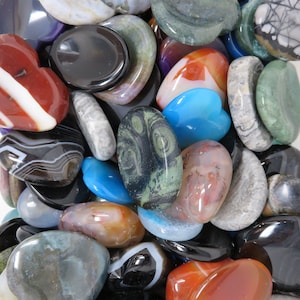 May include: A collection of polished heart-shaped and oval-shaped stones in various colors, including red, blue, green, black, and white. The stones are smooth and have a natural, polished finish.