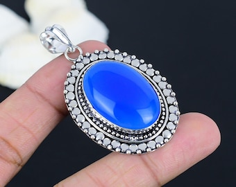 May include: Oval-shaped pendant with a vibrant blue gemstone set in a silver-toned metal frame. The gemstone is the focal point, surrounded by a detailed border. The pendant has a decorative bail for a chain.
