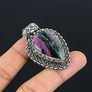 May include: A teardrop-shaped pendant with a silver setting. The pendant features a large, polished gemstone with purple and green hues. The setting has an ornate, filigree design around the stone.