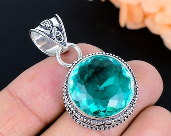 Puede incluir: Un colgante redondo de piedra preciosa color verde azulado facetada, engastado en un marco decorativo de plata esterlina. El engaste de plata presenta intrincados patrones de metal en los bordes y una gran argolla pulida en la parte superior.