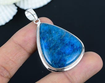 May include: A teardrop-shaped pendant with a vibrant blue gemstone set in a silver-colored metal frame. The gemstone has a textured appearance, and the pendant includes a small loop for a chain. The background is dark.