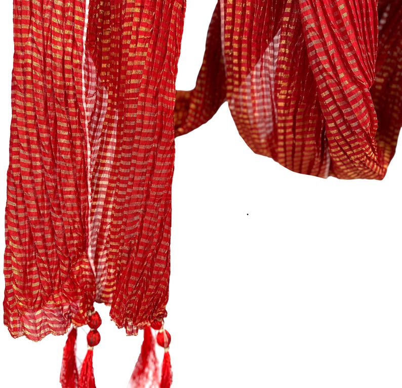 May include: A red scarf with a gold checkered pattern and red tassels. The scarf is made of a lightweight fabric and has a flowing design. The tassels are attached to the bottom edge of the scarf.