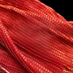 May include: A vibrant red fabric with a gold checkered pattern. The fabric is draped, creating folds and shadows that highlight the texture and design. The gold accents add a touch of elegance to the overall look.