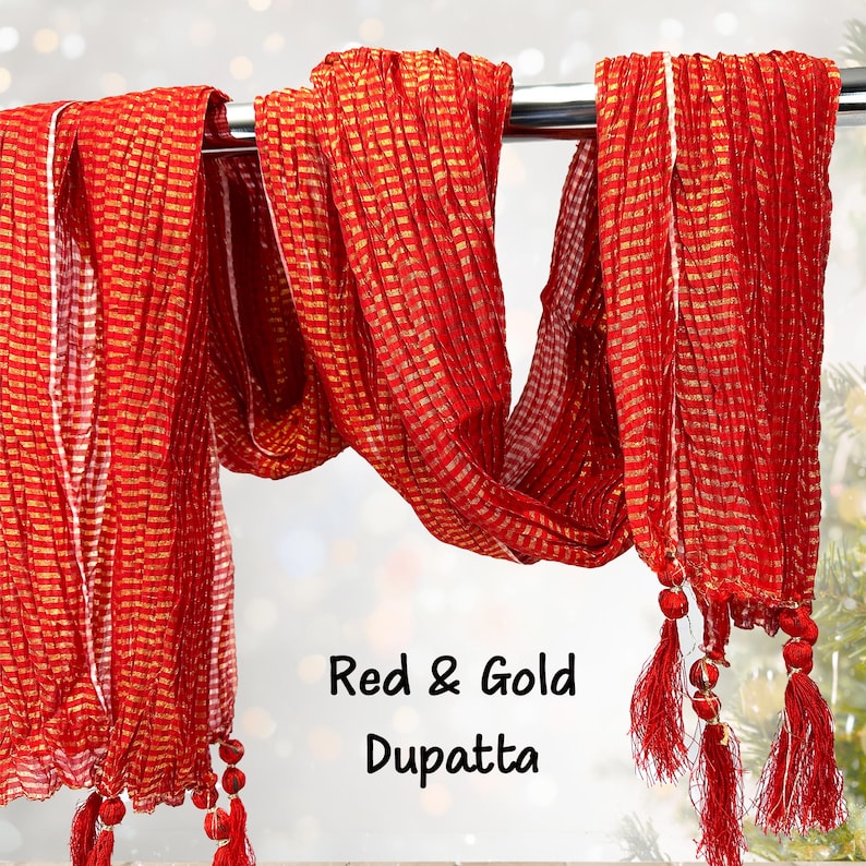 May include: A red and gold dupatta, a traditional Indian scarf, hangs from a metal rod. The scarf features a striped pattern with gold accents and red tassels at the ends. The text "Red & Gold Dupatta" is visible.