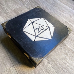 May include: A black wooden box with gold accents and a white 20-sided die design on the lid.