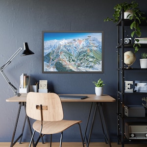 May include: A framed map of a ski resort, showcasing colorful ski runs against a backdrop of snow-capped mountains and a clear blue sky. The map is displayed on a dark blue wall above a wooden desk with a black lamp and a wooden chair.