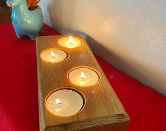 Pode incluir: Um porta-velas de madeira com quatro ranhuras para velas votivas. O porta-velas é feito de madeira natural e tem um aspecto rústico. As velas estão acesas e brilham.