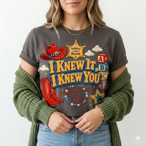 Pu&ograve; includere: Una t-shirt grigio scuro con una stampa grafica raffigurante un cappello da cowboy rosso, una stella da sceriffo gialla con il testo Infinity and Beyond, stivali da cowboy rossi, cubi dell'alfabeto e un braccialetto di perline.