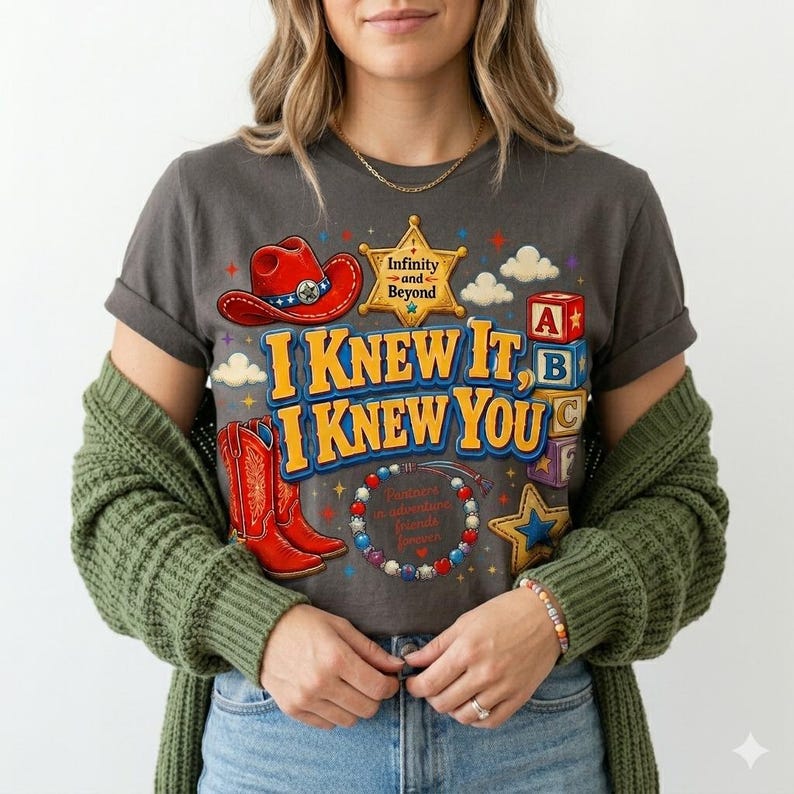 Pu&ograve; includere: Una t-shirt grigio scuro con una stampa grafica raffigurante un cappello da cowboy rosso, una stella da sceriffo gialla con il testo Infinity and Beyond, stivali da cowboy rossi, cubi dell'alfabeto e un braccialetto di perline.
