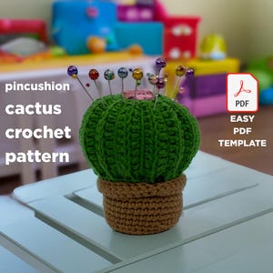May include: A green crocheted cactus pincushion with a brown crocheted pot. The cactus is decorated with colourful pins. The image includes the text "pincushion cactus crochet pattern EASY PDF TEMPLATE".