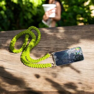 May include: A bright green braided phone strap with gold metal rings and a clear phone case with a reflection of a cloudy sky and palm trees.