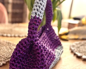 May include: A small, purple and silver crocheted handbag with a silver handle.