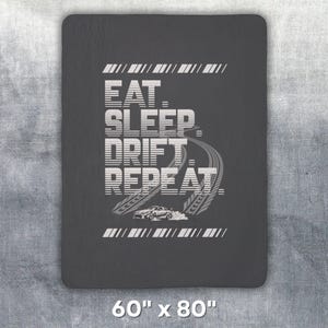 May include: Dark gray blanket with the text "EAT. SLEEP. DRIFT. REPEAT." in white, along with a graphic of a drifting car and tire tracks. The blanket measures 60 inches by 80 inches.