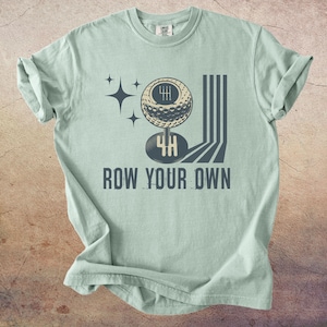 May include: A light green t-shirt with a graphic design featuring a golf ball-shaped gear shift, the number 4H, and the text "ROW YOUR OWN". The design includes star shapes and vertical lines.