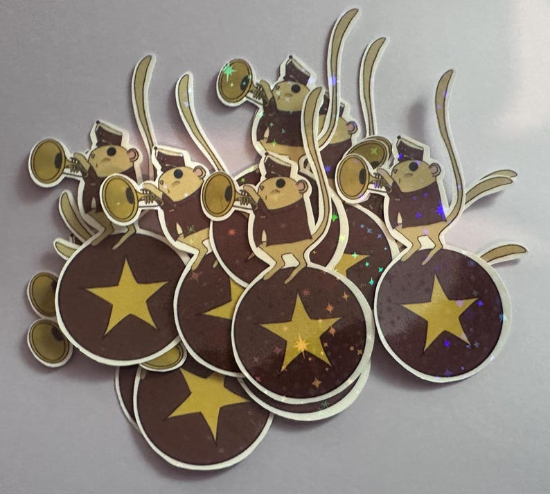 May include: A collection of stickers featuring cartoon monkeys playing trumpets atop brown orbs with gold stars. The monkeys wear brown jackets and hats. The orbs have a sparkly, iridescent effect.