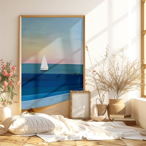May include: A framed print of a seascape with a sailboat in the distance. The print is hanging on a white wall above a white bed with a white pillow and a white blanket. There is a small potted plant on the bed and a gold picture frame on the floor.