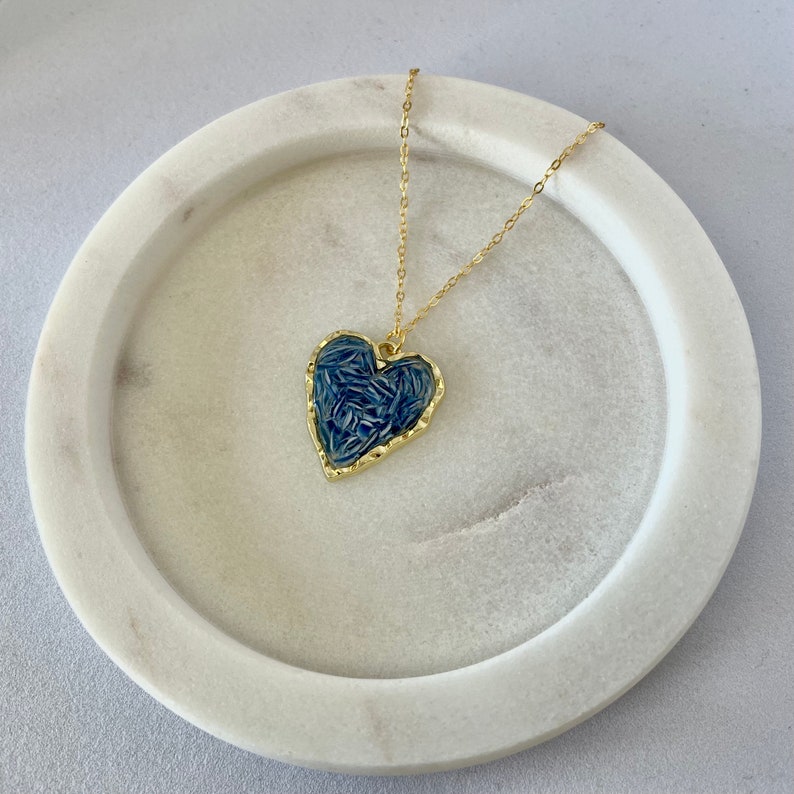 May include: A gold chain necklace with a blue heart pendant. The heart has a textured design and a gold border.