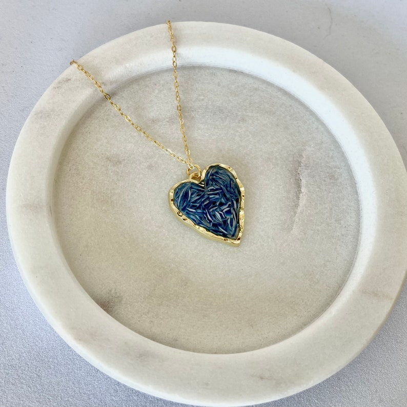 May include: A gold chain necklace with a blue heart-shaped pendant. The pendant is filled with a textured pattern of blue.