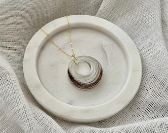 May include: A gold chain necklace with a pendant made of multiple layers of hair encased in clear resin, forming a circle shape.