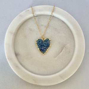 May include: A gold chain necklace with a blue heart pendant. The heart is textured and has a gold border.