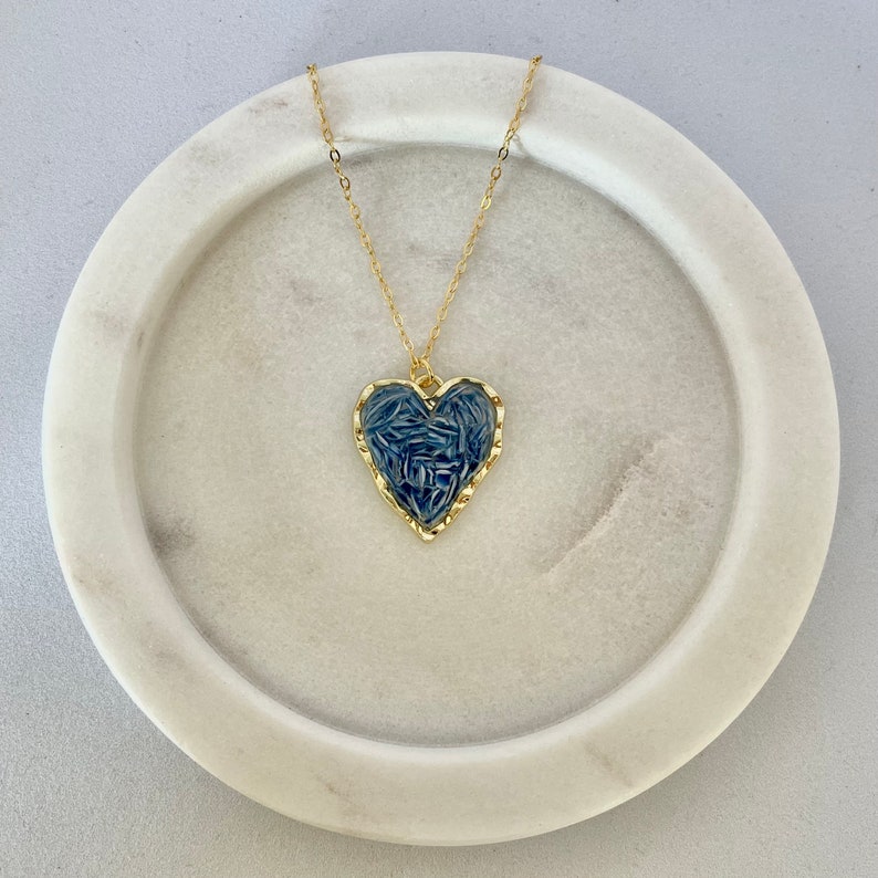 May include: A gold chain necklace with a blue heart pendant. The heart is textured and has a gold border.