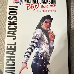 Pode incluir: Capa de DVD do "Bad Tour 1988" de Michael Jackson ao vivo em Roma e Tóquio. A capa mostra Michael Jackson em um traje prateado e preto, segurando um microfone. O logotipo da Pepsi é visível.