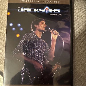 May include: DVD case for "The Jacksons: Triumph Live" featuring a live performance image. The cover displays the band's name and the title. The image shows a man in a sequined shirt singing into a microphone.
