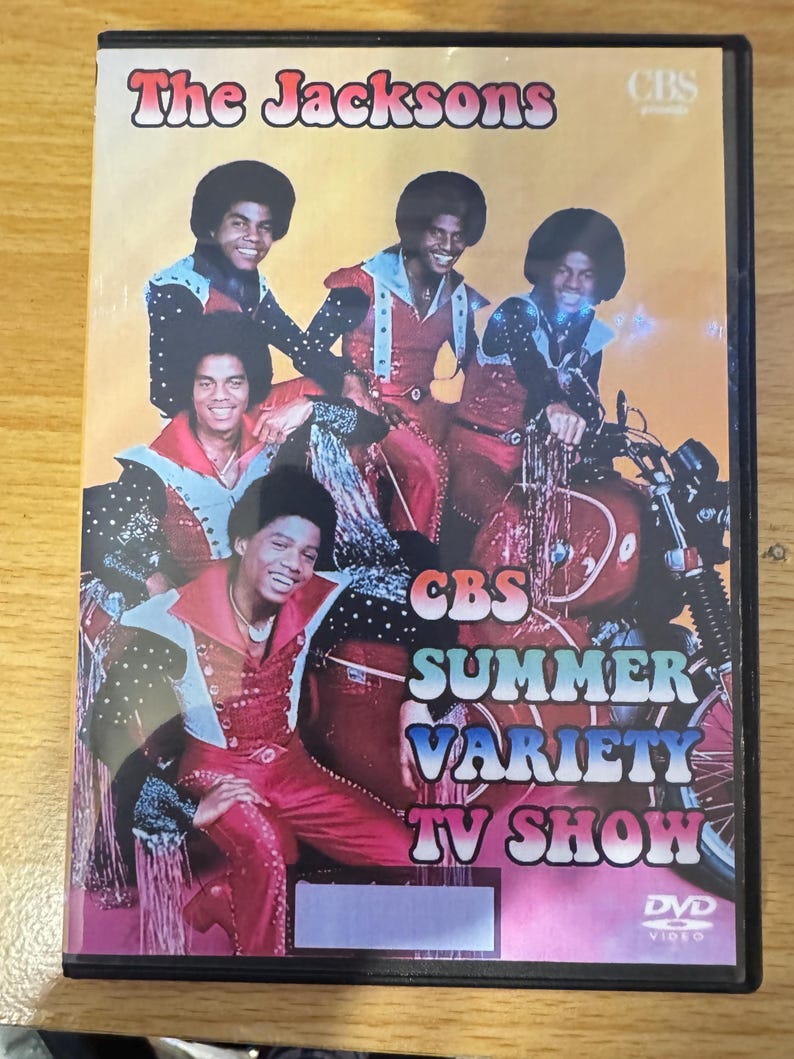 Puede incluir: Car&aacute;tula de DVD con The Jacksons en un programa de variedades de verano de CBS. La portada presenta una foto de la banda con atuendos coloridos, con una motocicleta en el fondo. El texto "CBS Summer Variety TV Show" est&aacute; impreso en letras grandes y coloridas.