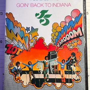 May include: A DVD case for The Jackson Five Goin' Back to Indiana featuring a colorful graphic illustration of the band performing on stage with comic book style text bubbles reading ZOT and VAROOOM against a white background.