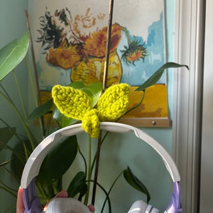 May include: White headphones with purple accents and a bright yellow crocheted butterfly charm attached to the headband.