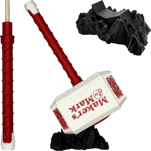 May include: A decorative hammer in white and red, featuring the text "Maker's Mark" in red. The hammer rests on a black rock-like base. A separate red handle is also visible.
