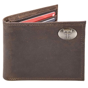 Puede incluir: Una cartera de cuero marrón con un emblema plateado con una letra "T" estilizada. La cartera está abierta, revelando ranuras para tarjetas con tarjetas visibles. Los bordes están cosidos con un hilo en contraste.