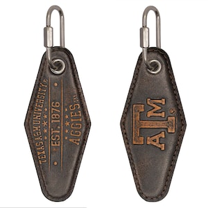 May include: A pair of brown leather keychains with a metal clasp. One keychain features the text "TEXAS A&M UNIVERSITY EST. 1876 AGGIES". The other keychain has the letters "A&M".