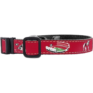 May include: Red dog collar featuring a repeating pattern of a football stadium, a bulldog, and a football helmet. The collar has a black buckle and a black adjustable strap. The collar is designed for a pet.