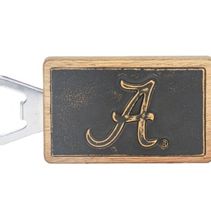 Puede incluir: Un abridor de botellas de madera con un logotipo de Alabama 'A' en negro y dorado. El abridor está hecho de madera y tiene un abridor de botellas de metal.