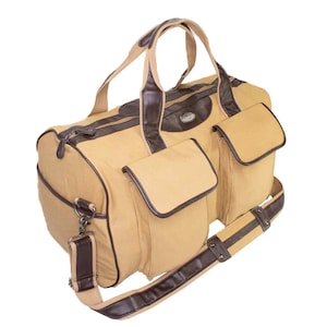May include: Tan duffel bag with brown leather accents. Features include two front pockets, a top zipper, and a detachable shoulder strap. The bag has two top handles and a brown leather trim.
